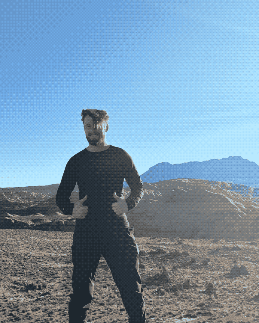 Toby in the Utah desert, two thumbs up, red rock and a blue peak behind